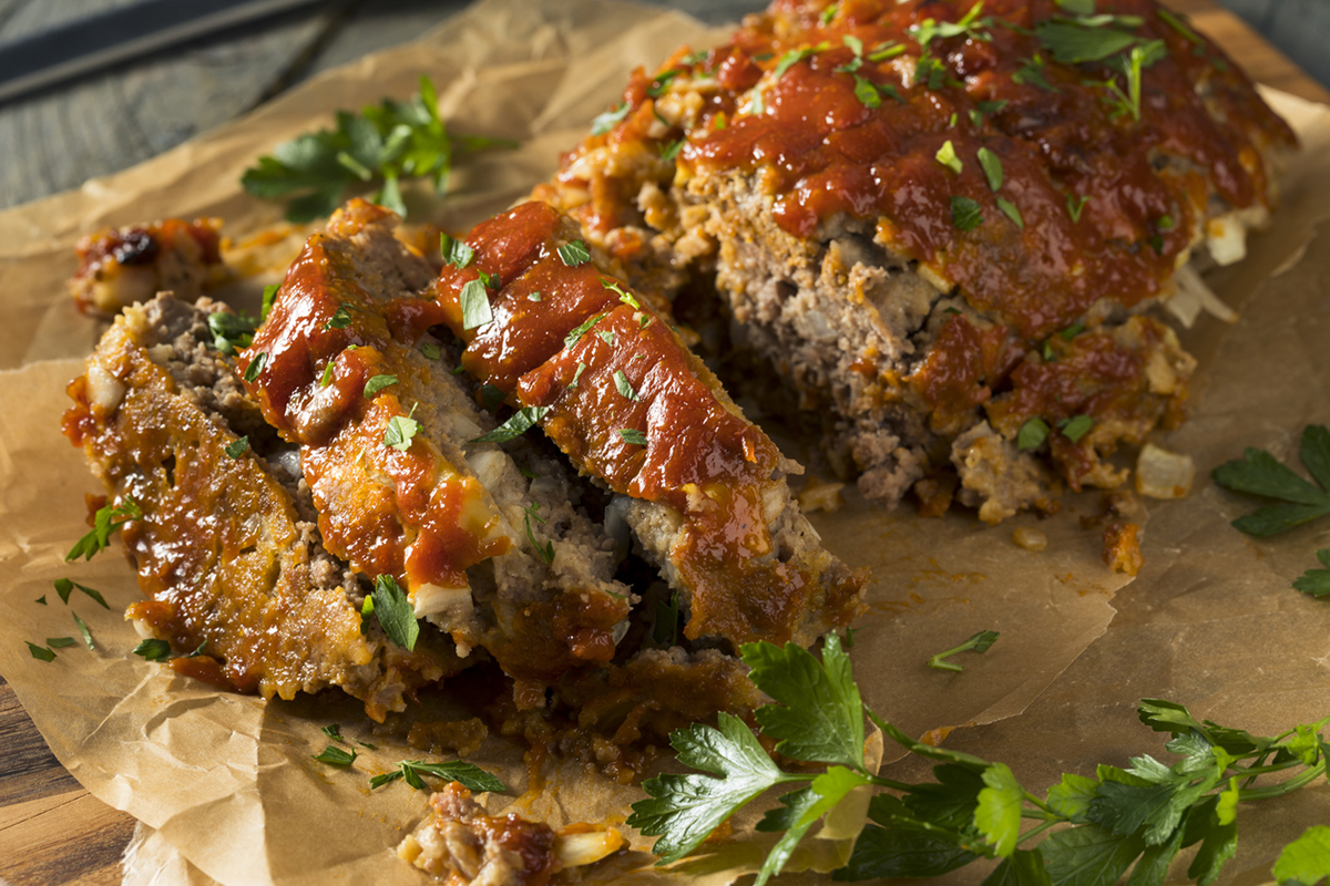 Meatloaf topped with ketchup and chopped parsley. Sitting on parchment paper and wooden cutting board.