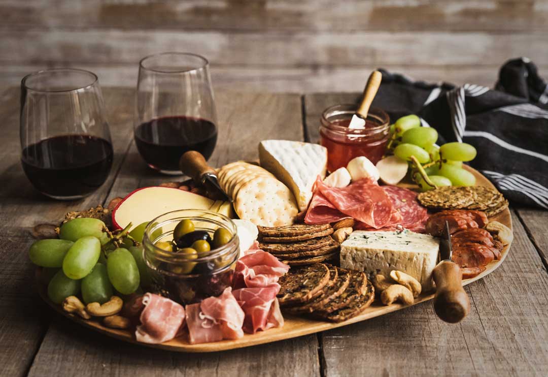 Charcuterie board with luscious grapes, red wine, cheeses, nuts, and salami