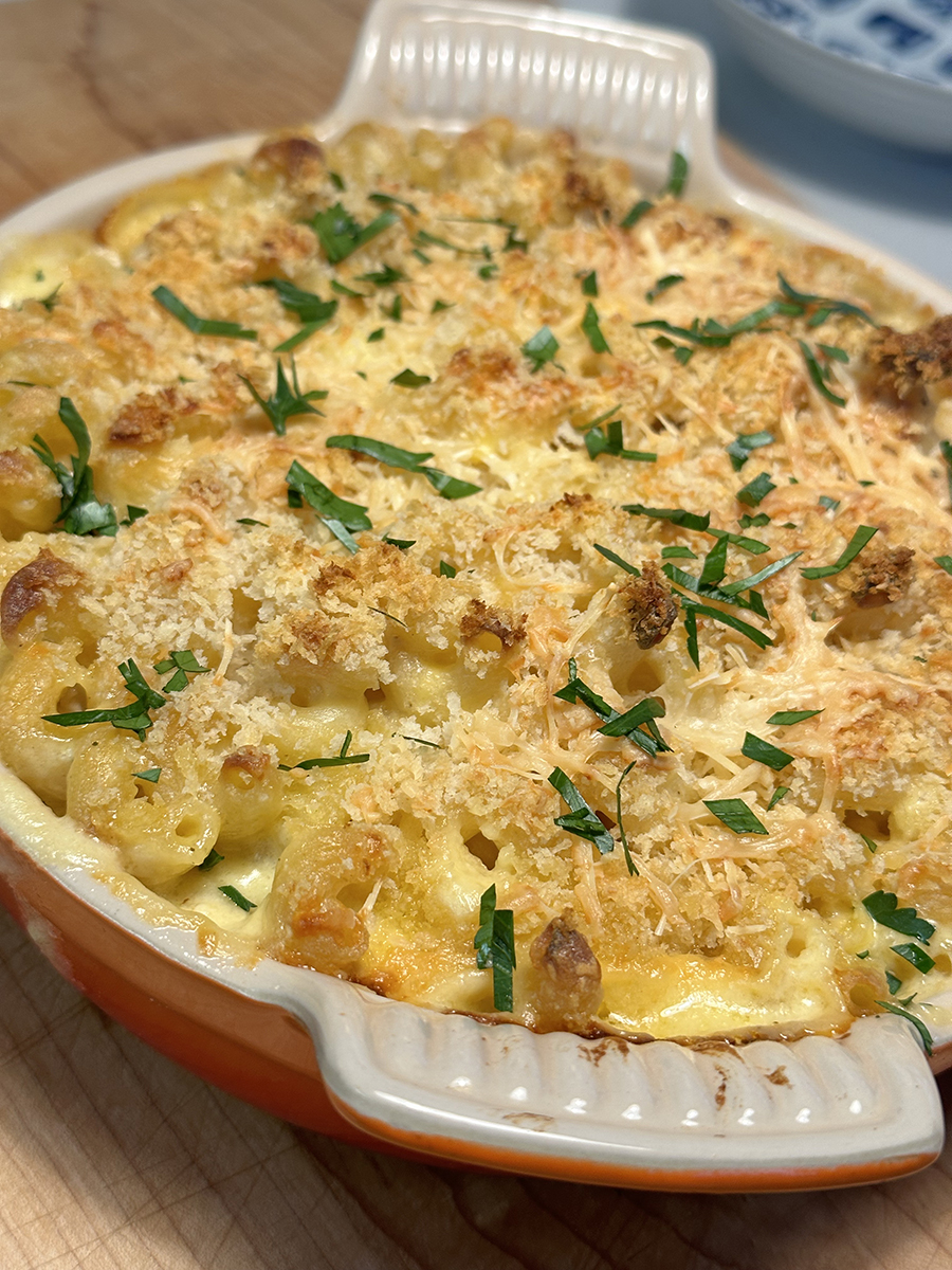 Macaroni and Cheese Casserole topped with cheesy breadcrumbs and chopped parsley, in an orange and white casserole dish.