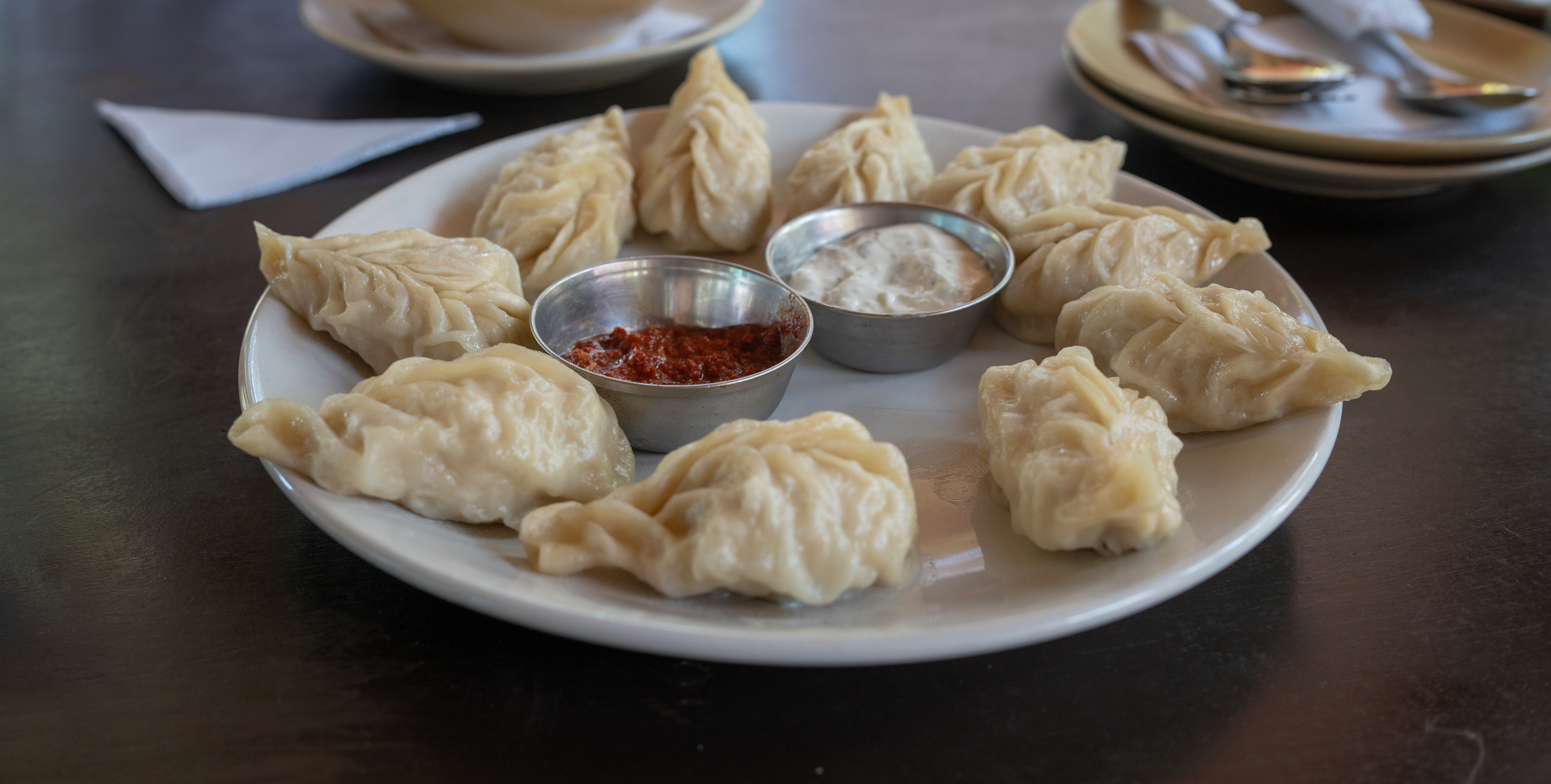 White plate full of Tibetan Momo dumplings, circling little dishes of dipping sauces.