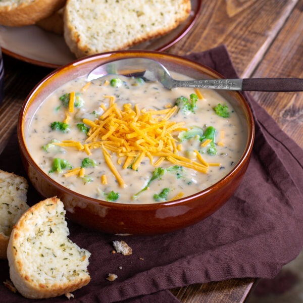 Bowl of creamy broccoli cheddar cheese soup with toasted cheese bread on a wooden table