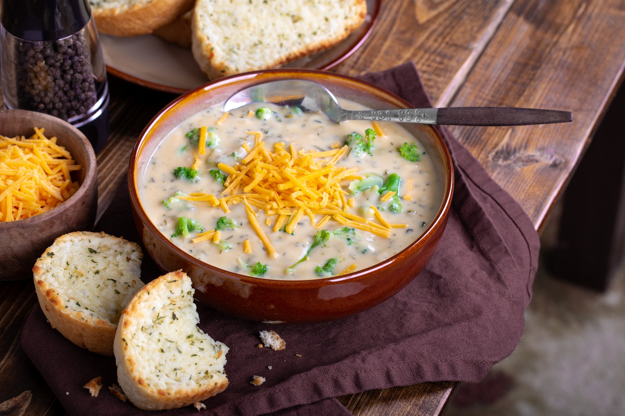 Bowl of creamy broccoli cheddar cheese soup with toasted cheese bread on a wooden table