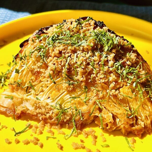 Roasted green cabbage wedge with breadcrumbs and chopped parsley. Yellow plate and blue tablecloth.