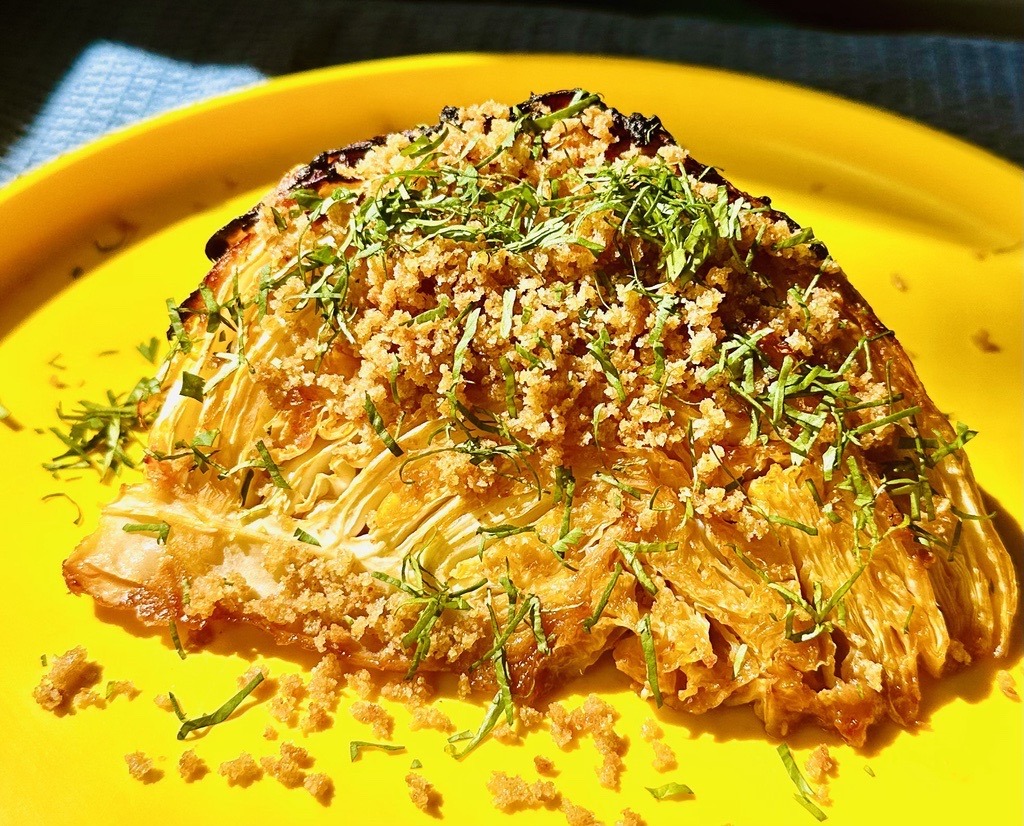 Roasted green cabbage wedge with breadcrumbs and chopped parsley. Yellow plate and blue tablecloth.