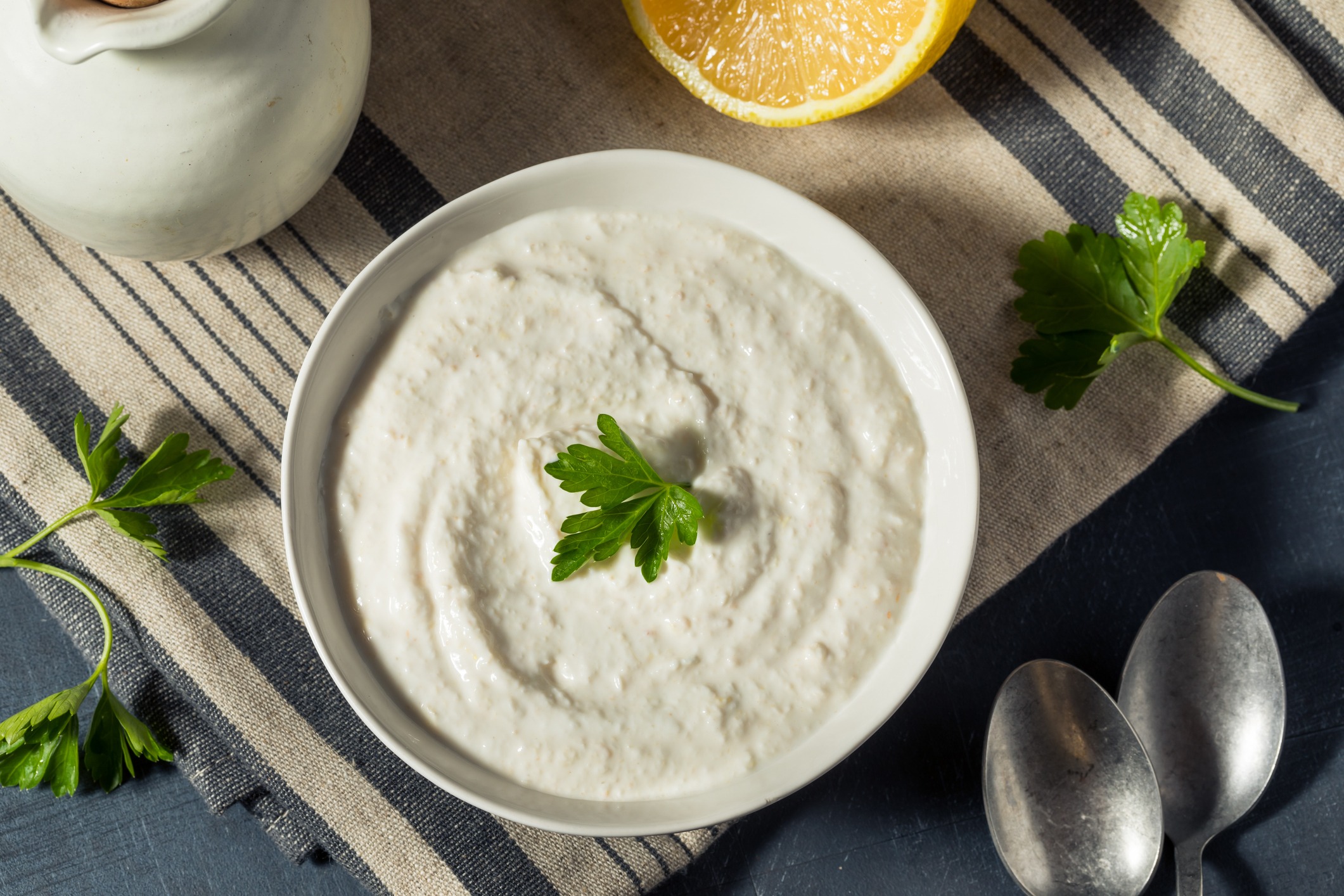 Horseradish Cream Sauce in a white bowl. Sitting on a striped white and black tablecloth, with parsley and lemon garnish to the side.