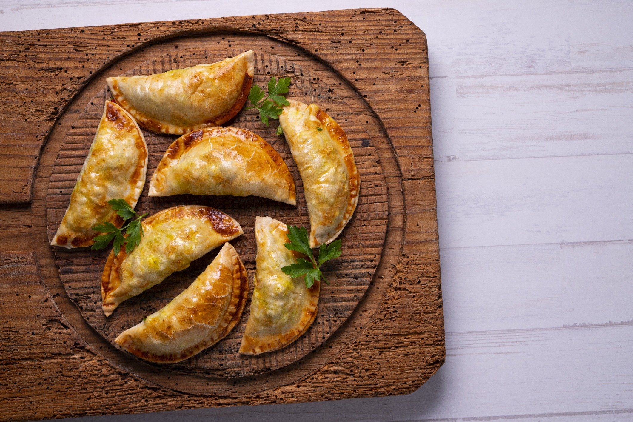 Empanadas - hand held pastries stuffed with corned beef, cabbage, carrots, potatoes and Swiss cheese for St. Patrick's Day. Garnished with parsley and sitting on a brown wooden serving board.