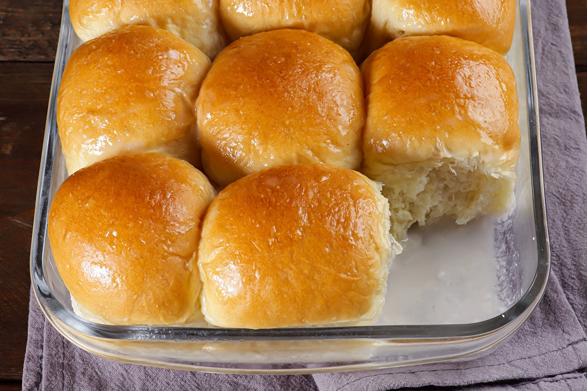 Shiny rows of rolls in a glass baking pan. Sitting on top of sweet coconut milk. Gray napkin underneath.