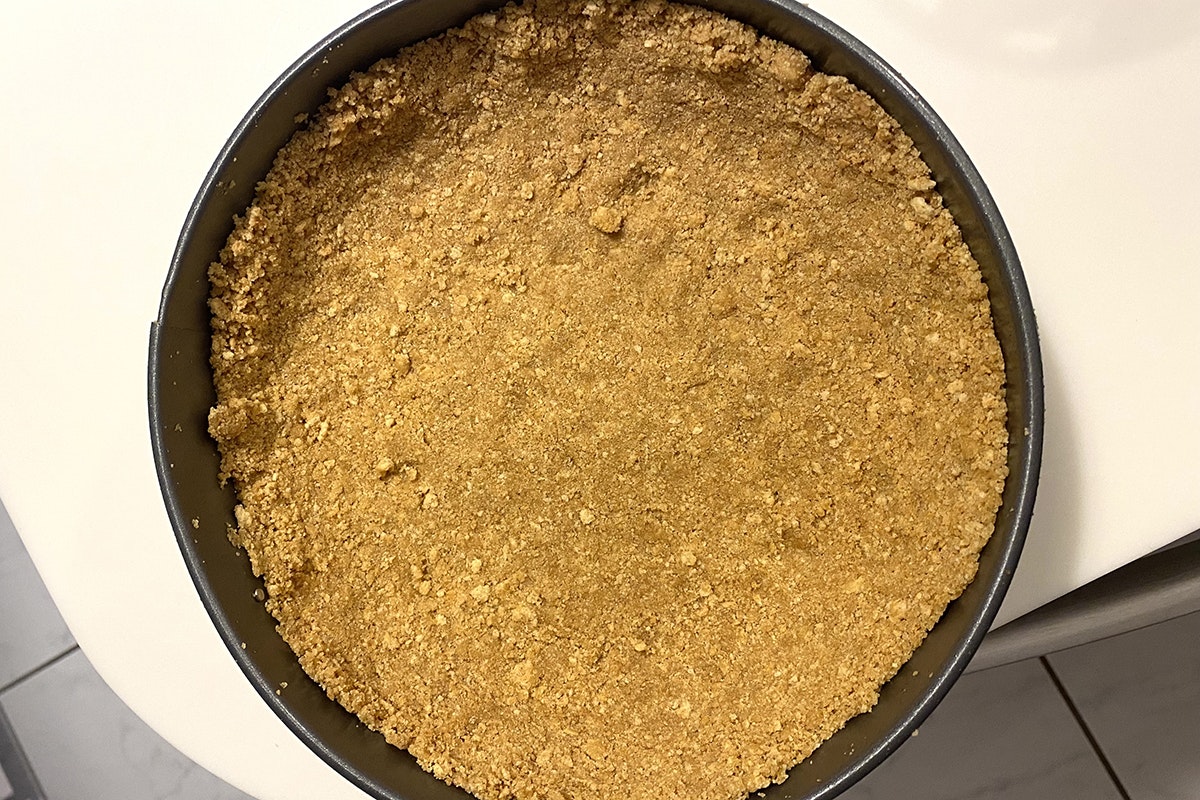 Pie crust in dark gray metal pie pan, made of pretzel crumbs pressed into the pan. On white table.