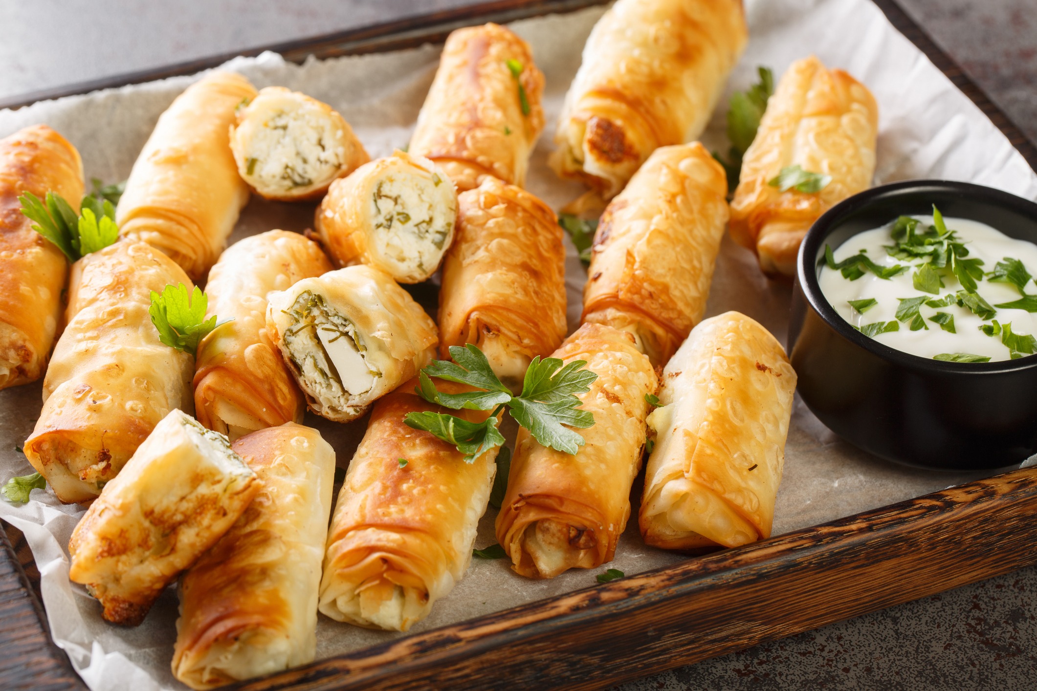 Rolled, baked phyllo dough with herbs and cheese inside. Dip of yogurt and herbs on the side. All in a wooden tray lined with paper.