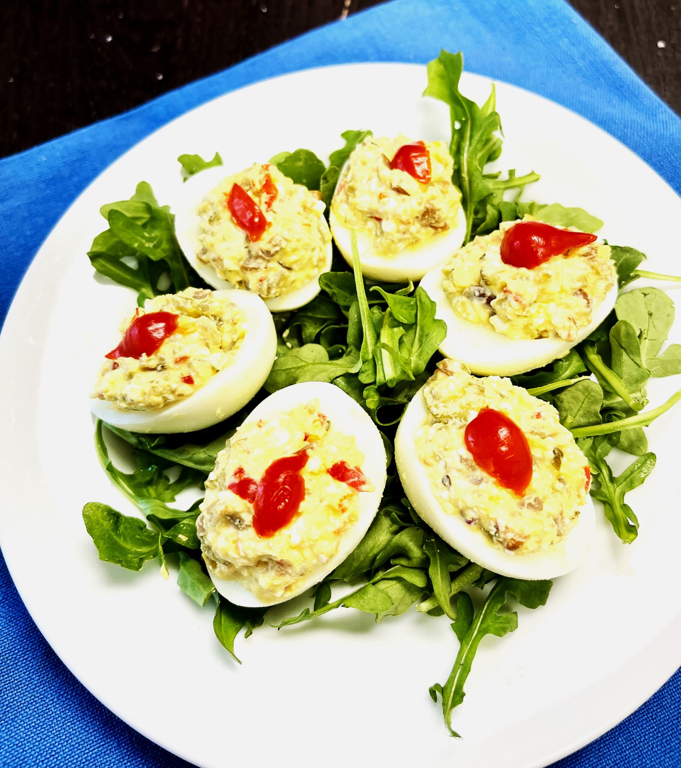 Deviled eggs made with cornichons, marinated peppers, mushrooms and olives. Six in a circle atop bed of arugula greens.