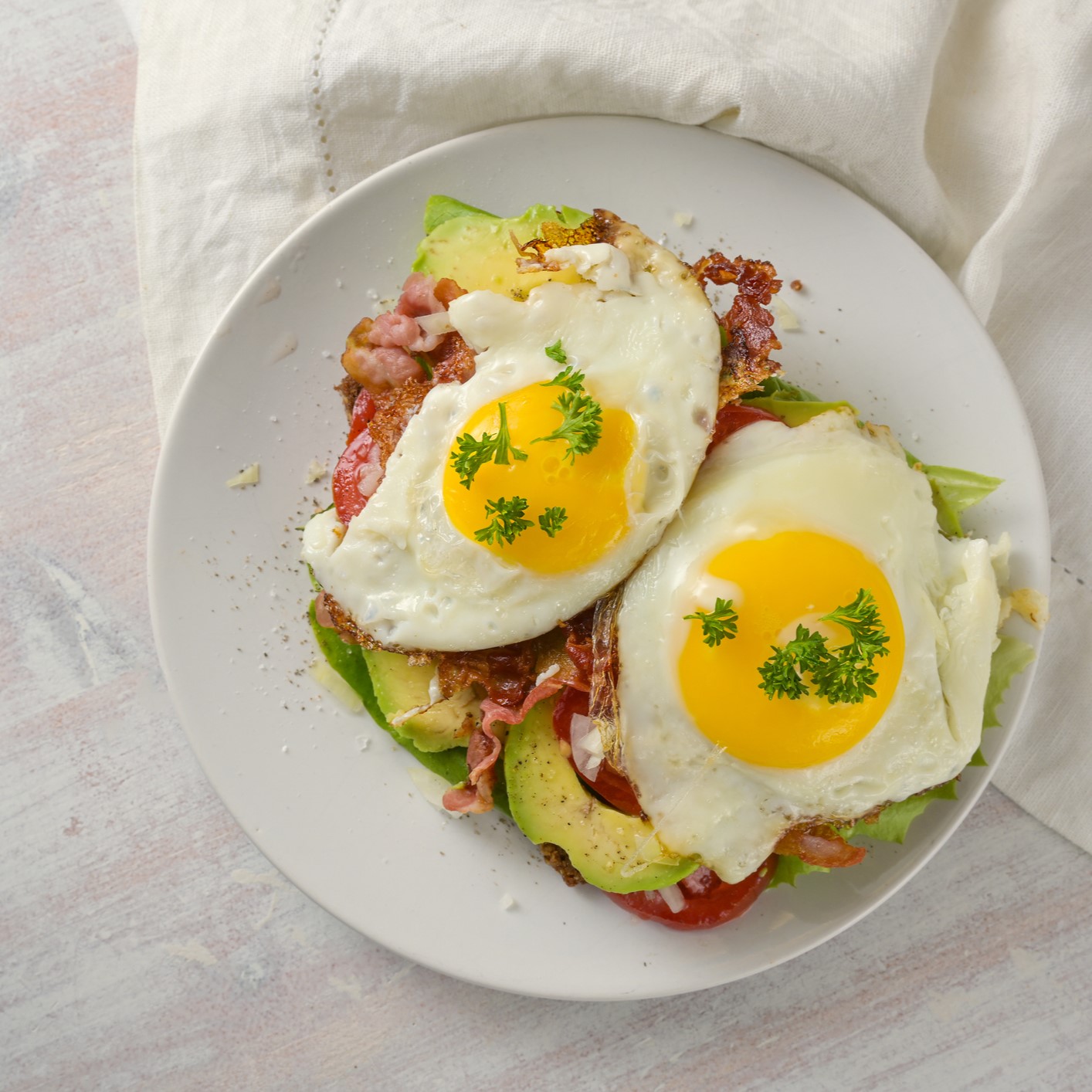 BLT with fried egg and avocado. White plate, napkin and wooden background.