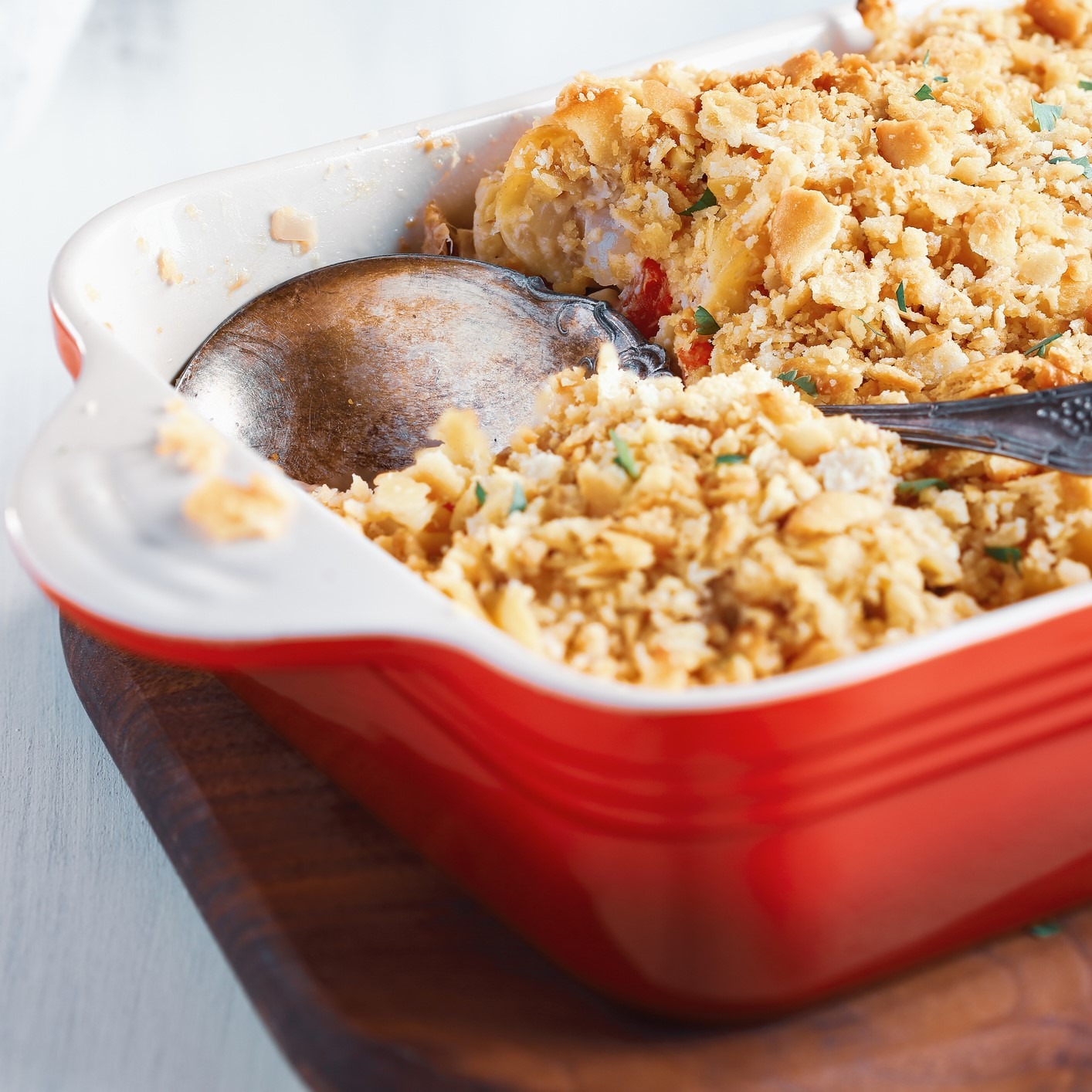 Chicken and veggie casserole with crumbled cracker top. Red casserole dish and big silver serving spoon.