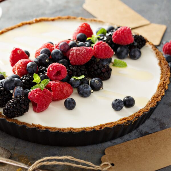 Yogurt Pie with Pretzel Crust and Fresh Fruit. In pie tin on gray surface. Fresh berries and mint sprigs.
