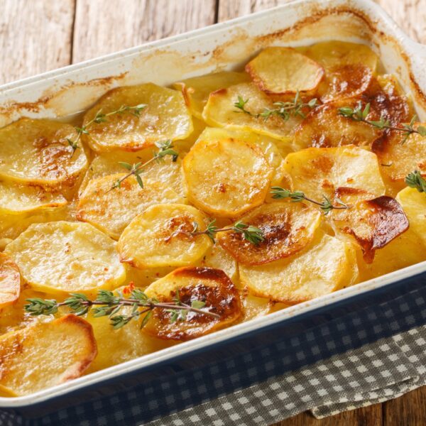 Casserole dish with layers of cooked potatoes. Brown and toasty on top, garnished with thyme sprigs.