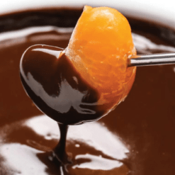 Mandarin section dipped in chocolate fondue sauce. On a fondue fork.