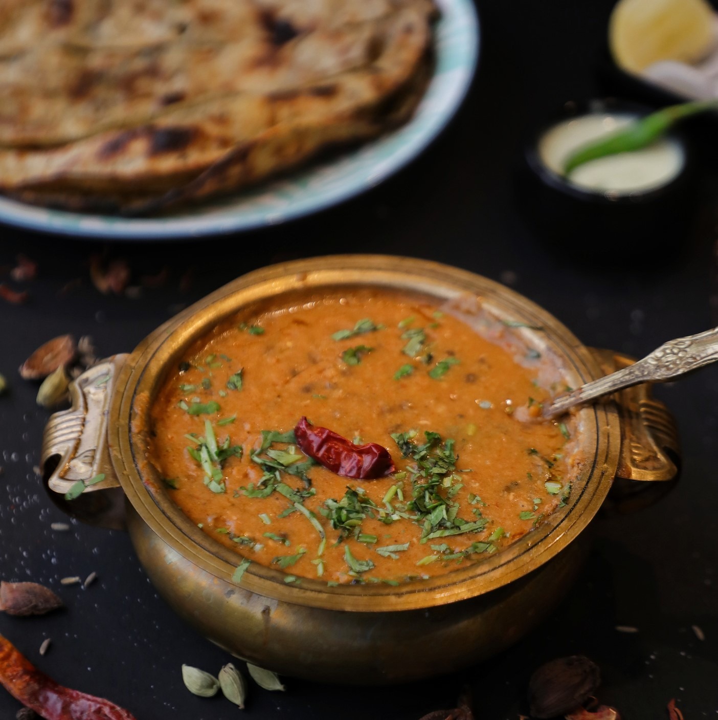 Bowl of lentil and mung dal soup, topped with choped herbs and a dried chili pepper. Table strewn with spice pods.