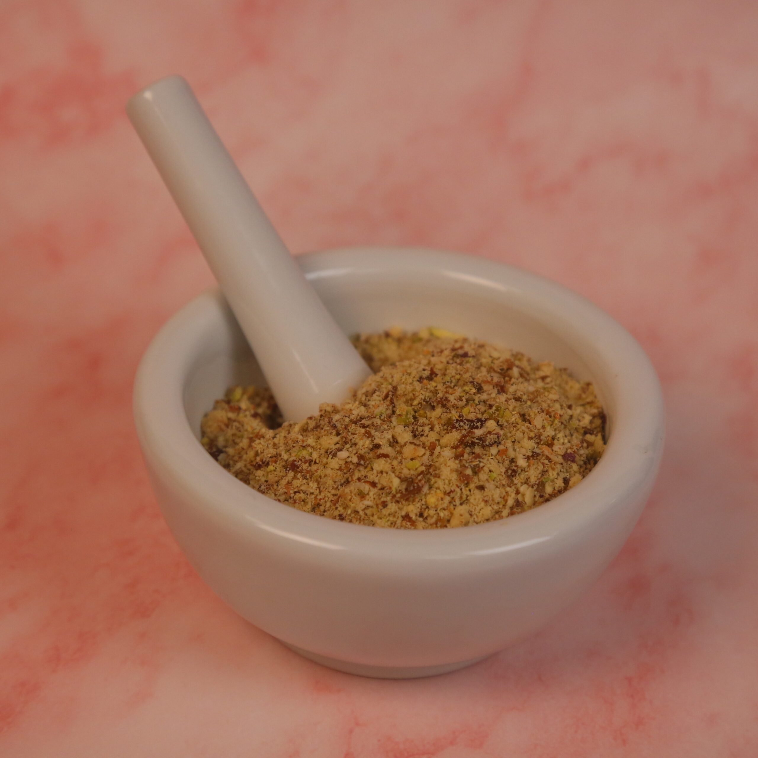 Ground spices and nuts in a mortar and pestle. Pink marble background.