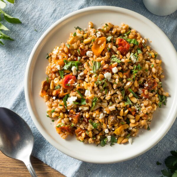 Farro salad with roasted and sundried tomatoes, feta cheese and chopped fresh herbs. White plate on a blue tablecloth.