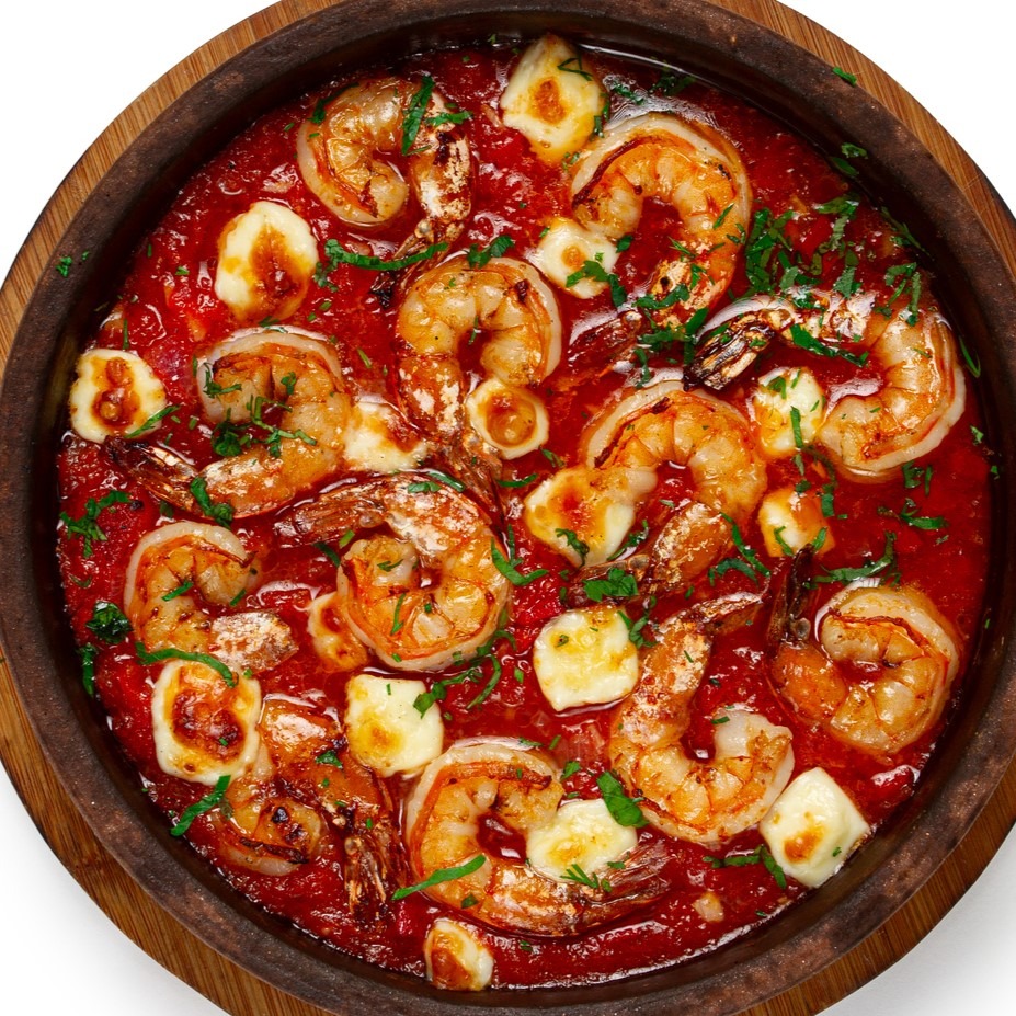 Greek Shrimp Saganaki - Wooden serving bowl with shrimp, feta cheese and fresh herbs in a tomatoey sauce