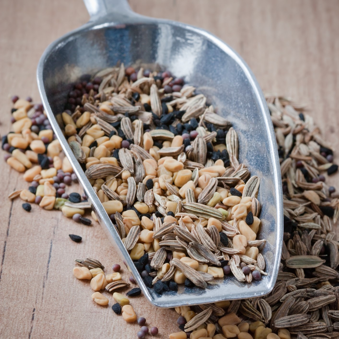 Shiny metal scoop filled with whole spices. Wooden table.