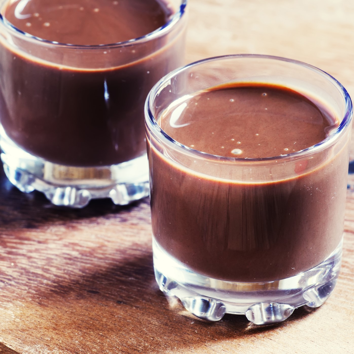 Heavy-bottom rocks glasses with thick hot cocoa. Wooden table.