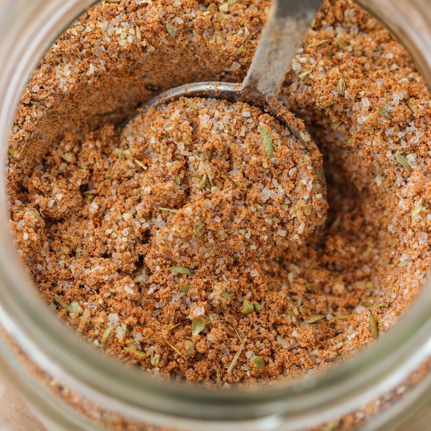 Combination of ground spices, dried herbs in a small glass jar. Top view with measuring spoon scooping the mixture.