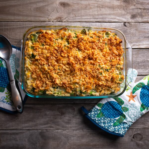 Casserole with crunchy cracker top, broccoli and cheese. Glass baking dish, wooden tabletop and ocean-themed oven mitt and potholder.