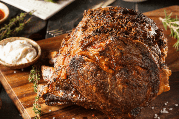 Beautifully cooked rib roast on a cutting board with herbs and a dish of horseradish