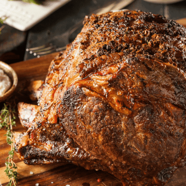 Beautifully cooked rib roast on a cutting board with herbs and a dish of horseradish