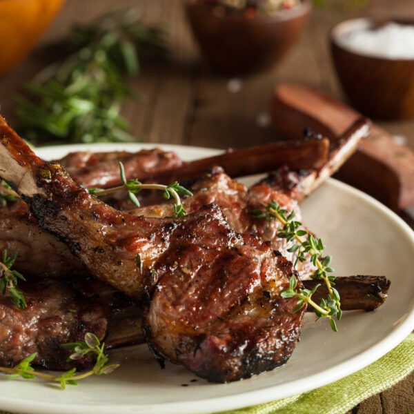 Grilled Lamb Chops with Thyme Sprigs. White plate, green napkin, wooden table with knife and small dish of salt.