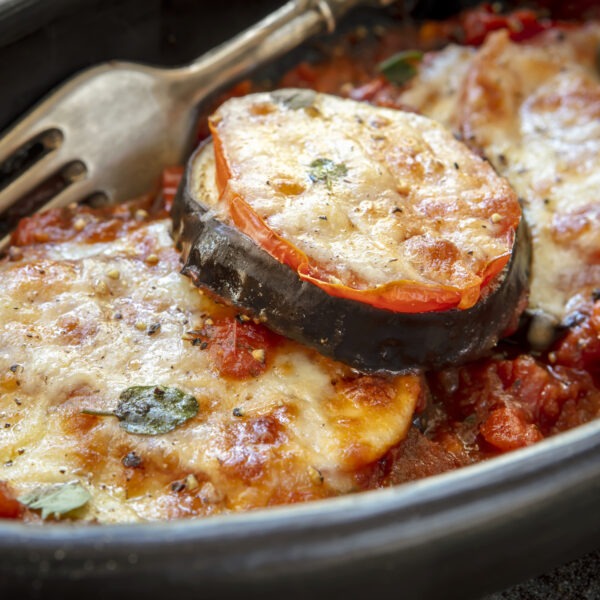Baked Eggplant Parmesan, with tomato and mozzarella, in black dish over slate.