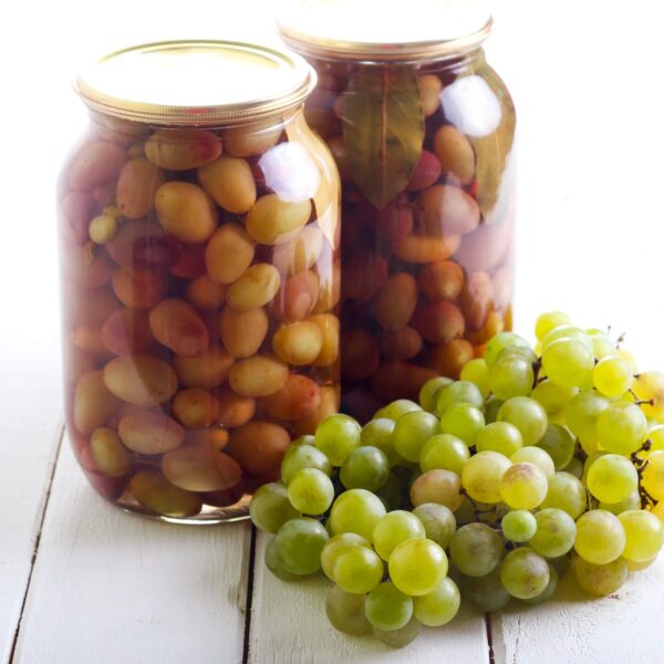 Sealed mason jars filled with pickled grapes on white painted wood slats and a bunch a fresh grapes