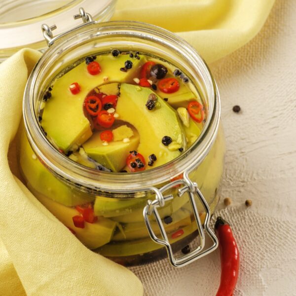 Glass jar filled with slices of ripe avocado, fresh chili pepper and black peppercorns