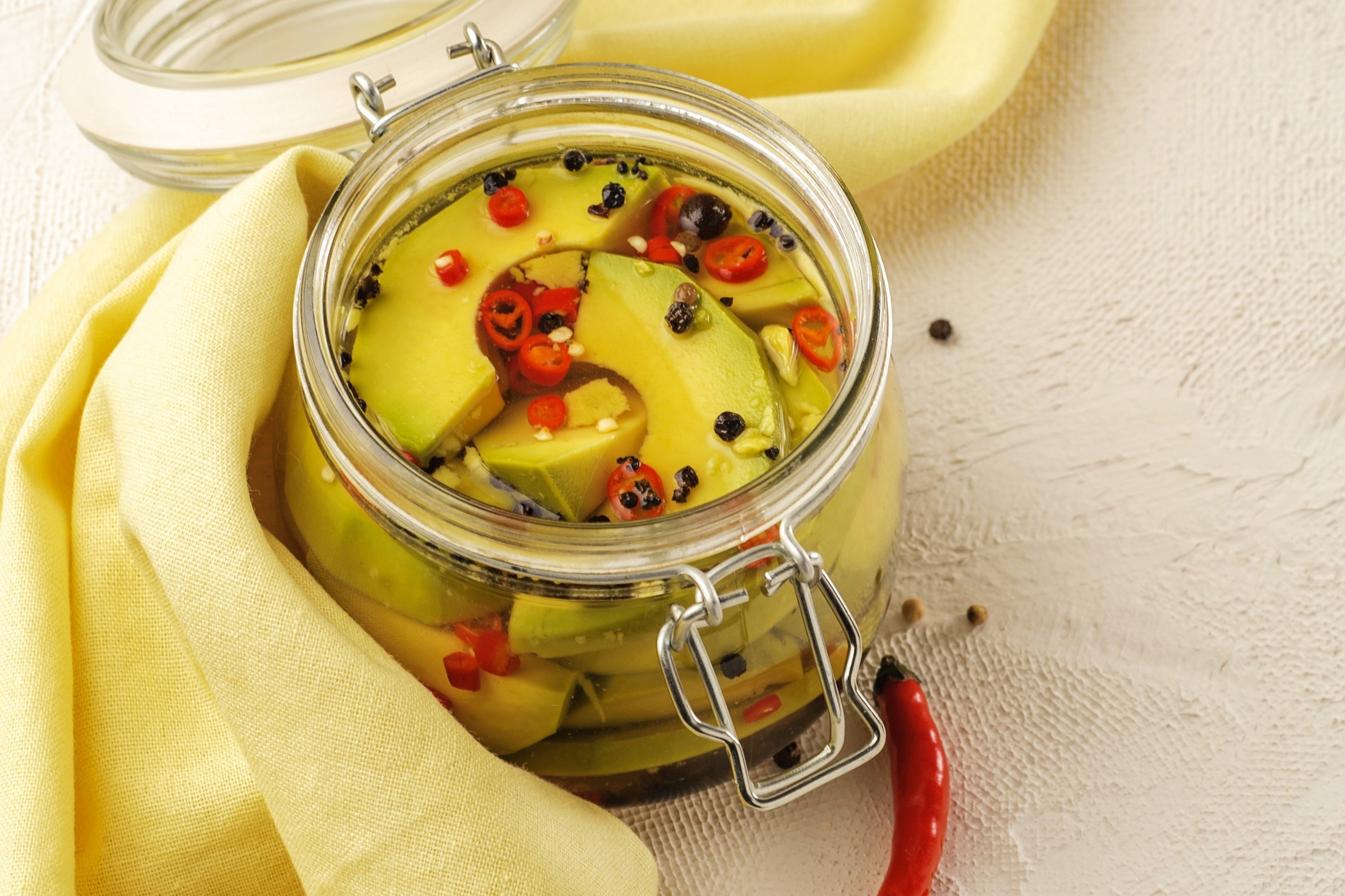 Glass jar filled with slices of ripe avocado, fresh chili pepper and black peppercorns