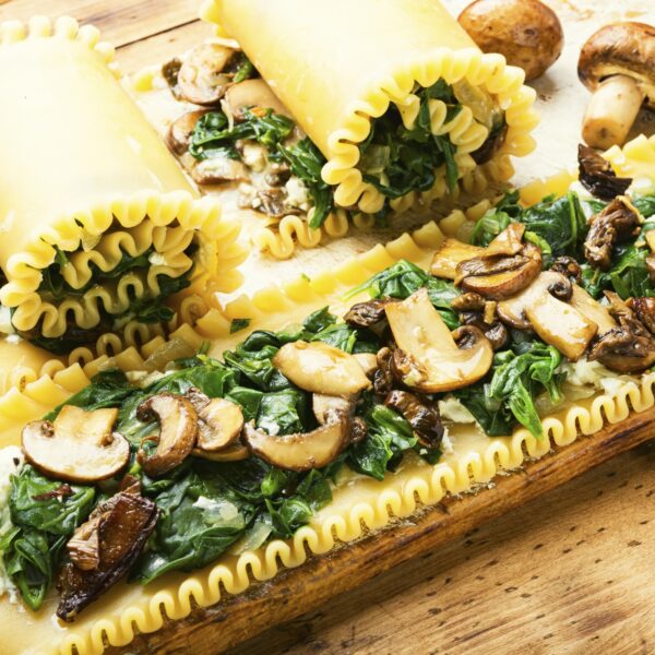 Lasagna noodles rolled up with filling of spinach and mushrooms. Wooden cutting board and table.