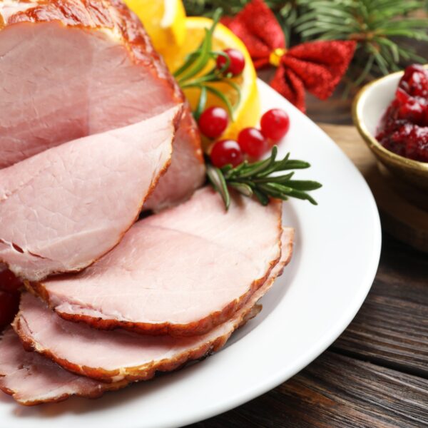 festive holiday ham sliced on a white plate with cranberries