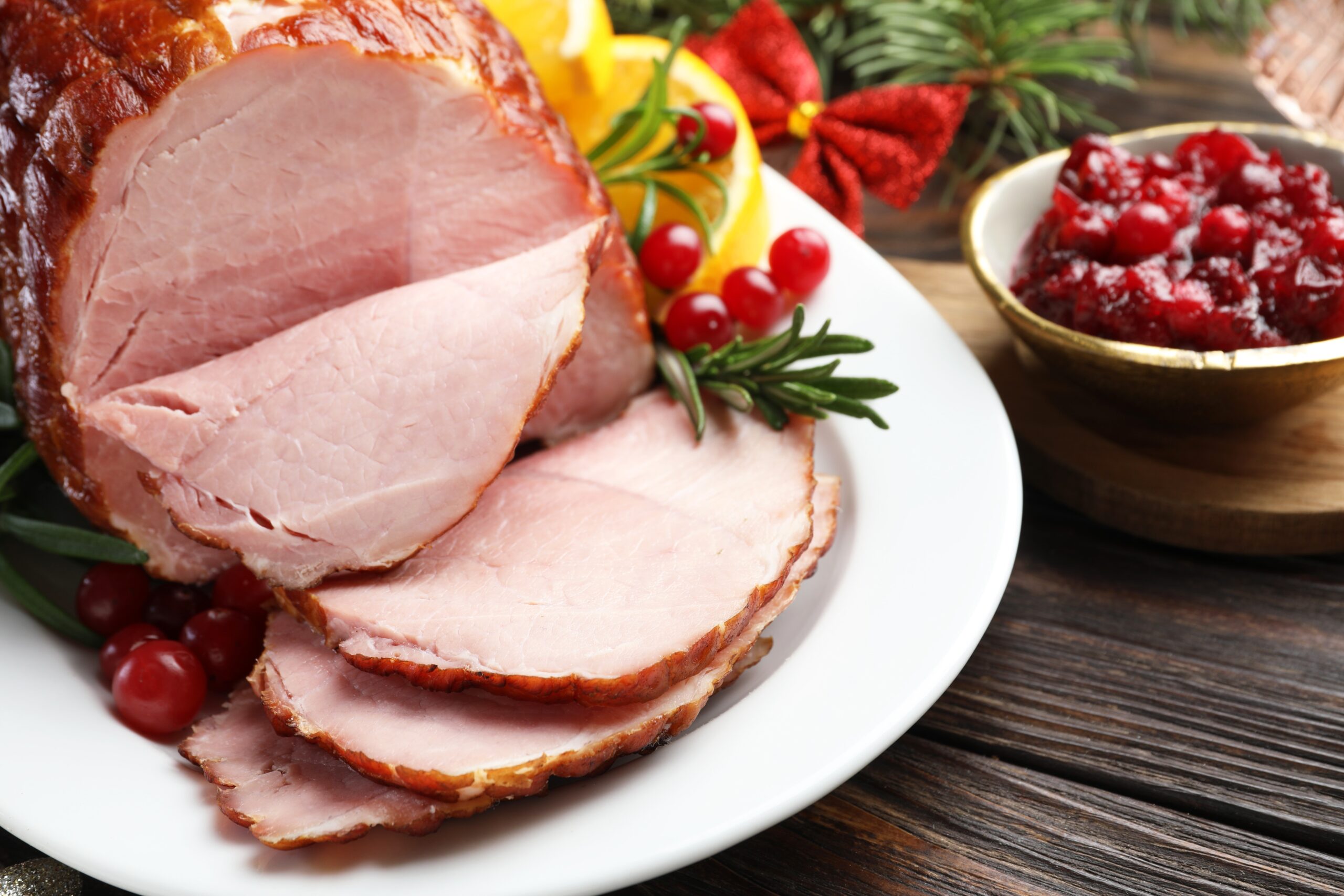 festive holiday ham sliced on a white plate with cranberries