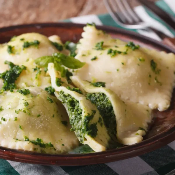 ricotta and pesto filled homemade raviolis on a rustic plate with green and white napkin