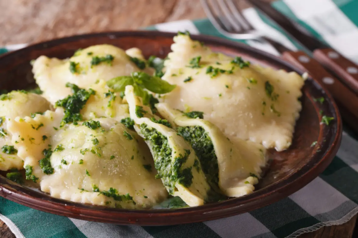 ricotta and pesto filled homemade raviolis on a rustic plate with green and white napkin